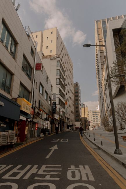 There is no image of flowers or floral arrangements in the provided picture; it depicts a city street with commercial buildings, signage, and streetlamps under a partly cloudy sky. The scene includes