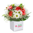 Infused with a joyful, uplifting feel that seems to echo Marks Gate's bright mornings and friendly streets, this bouquet is expertly arranged in a chic white gift bag, perfect for hand-delivery to someone special along Whalebone Lane or near Chadwell Heath. Lush coral and blush-red carnations, with their trademark ruffled texture, mingle harmoniously with crisp white daisies whose vivid yellow-green centers evoke happiness and renewal. Tiny, ethereal baby's breath blossoms are scattered throughout, their miniature white clouds softening the look and adding an air of gentle celebration. Unopened buds edged with soft purple emerge gracefully from the left, introducing a hint of promise for days to come. The bouquet is circled by lush, glossy green leaves, giving the entire arrangement an elegant, rounded silhouette and a touch of organic vibrancy. Against a pure white background, every colour pops, drawing attention to the craft behind each floral placement. This arrangement feels at once joyful and refined-perfect for birthdays, thoughtful gestures, or to simply brighten a neighbour's day in Marks Gate-offering a memorable moment of beauty drawn from local tradition.